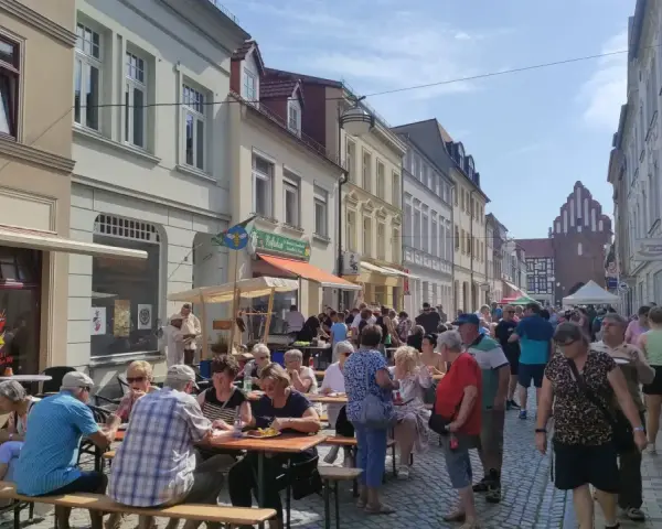 Menschen genießen ein Fest vor dem Kulturhaus Teterow. Viele sitzen an Tischen, essen und unterhalten sich.