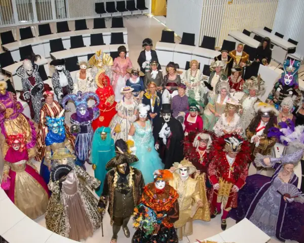 Eine Gruppe in prächtigen Kostümen und Masken, die an venezianische Tage in Schwerin erinnert, versammelt sich in einem modernen Sitzungssaal.