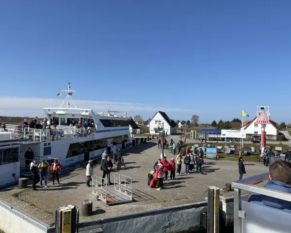 Menschen warten am Kai in Neuendorf auf Hiddensee auf die Fähre. Ein großes Ausflugsschiff liegt bereit.