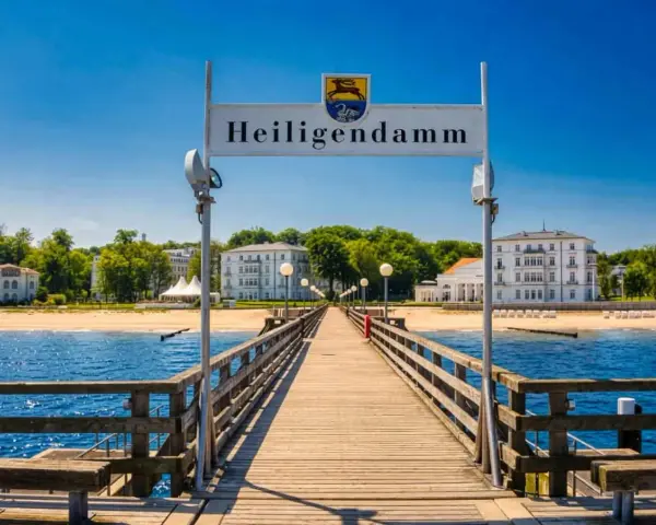 Holzsteg führt zum Heiligendamm Strand mit weißen Gebäuden und blauem Himmel.