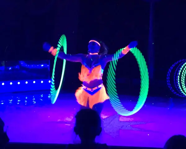 Artistin dreht leuchtende Reifen auf der Bühne des Circus Moreno. Neonfarben und Schwarzlicht erzeugen eine magische Atmosphäre.