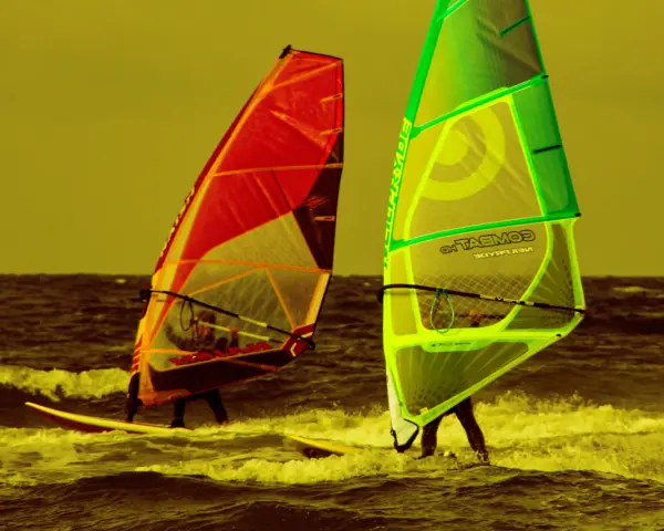 Zwei Windsurfer mit bunten Segeln auf dem Meer. Ein tolles Erlebnis für Surf und Segel Hiddensee.