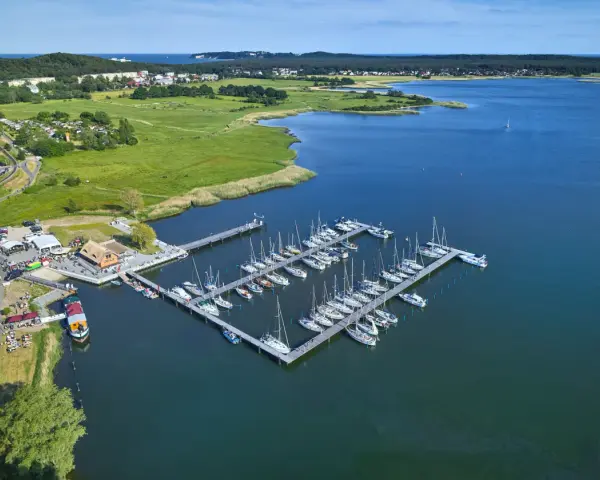 Der Hafen Sellin ist voller Segelboote, die auf dem ruhigen Wasser liegen. Im Hintergrund erstreckt sich eine grüne Landschaft mit Häusern und Bäumen.