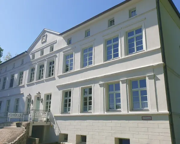 Das Herrenhaus Blengow, ein weißes Gebäude mit vielen Fenstern, steht unter blauem Himmel.