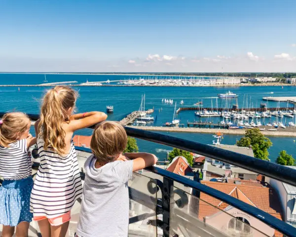Drei Kinder blicken auf einen belebten Hafen mit vielen Segelbooten. Ein schöner Tag für Veranstaltungen MV mit Kindern.