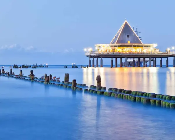 Ein beleuchteter Pier mit Restaurant und Wellenbrechern im Meer. Perfekt für einen Heringsdorf Urlaub.