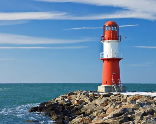 Roter Leuchtturm auf felsiger Mole am barth strand. Blaues Meer und Himmel mit Wolken.