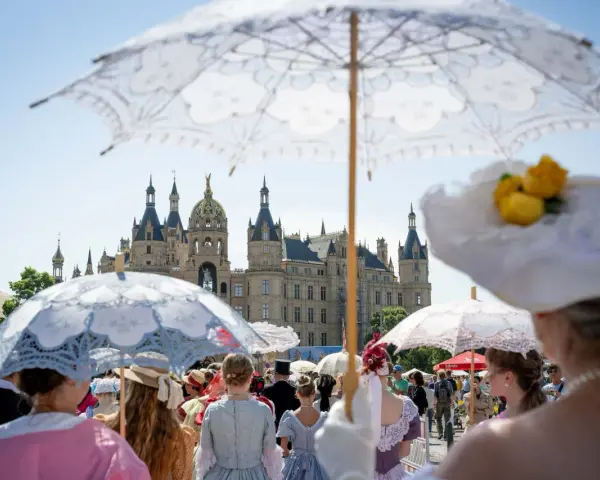 Besucher im historischen Gewand mit Sonnenschirmen beim Altstadtfest Schwerin vor dem Schloss.
