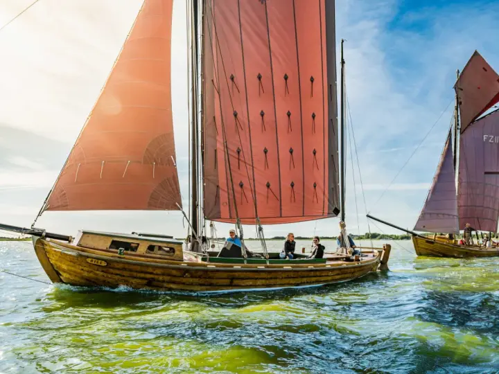 Zeesboot "Bill" segelt bei Ahrenshoop mit roten Segeln. Ein zweites Boot folgt.