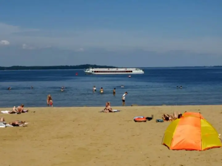 Sonne, Sand und ein Schiff auf dem Wasser – ein entspannter Tag am Schweriner Strand mit Badegästen und einer bunten Strandmuschel.