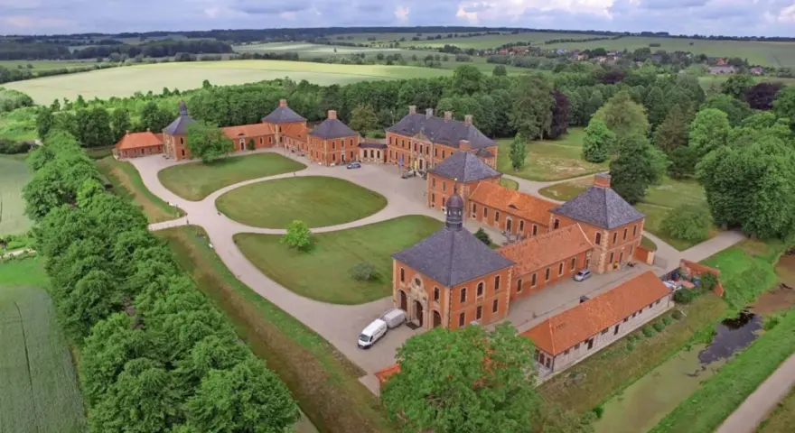 Luftaufnahme von Schloss Bothmer, einem barocken Anwesen mit roten Ziegelgebäuden, umgeben von grünen Gärten und Feldern.