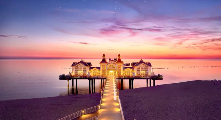 Pier mit beleuchtetem Gebäude im Abendrot, ein romantischer Blick auf die Sellin Innenstadt.