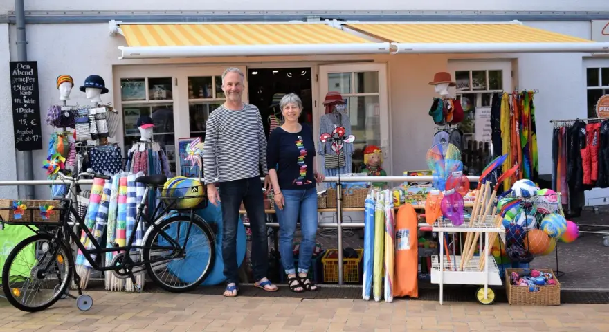 Ein Paar vor einem Laden mit Strandartikeln. Sie sind bereit, juliusruh einkaufen zu gehen und haben alles für einen schönen Tag am Meer.