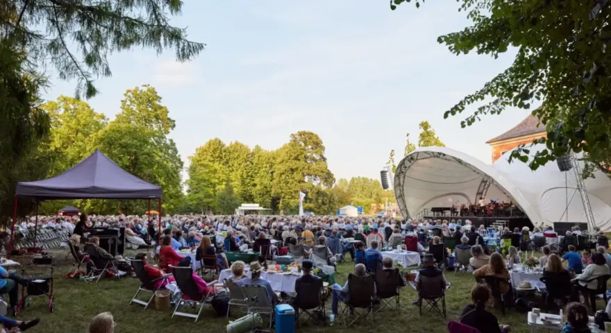 Großes Publikum bei einem Open-Air-Konzert im Rahmen eines **Festivals Mecklenburg-Vorpommern**. Eine Bühne mit Orchester, viele Sitzende auf Rasenflächen.
