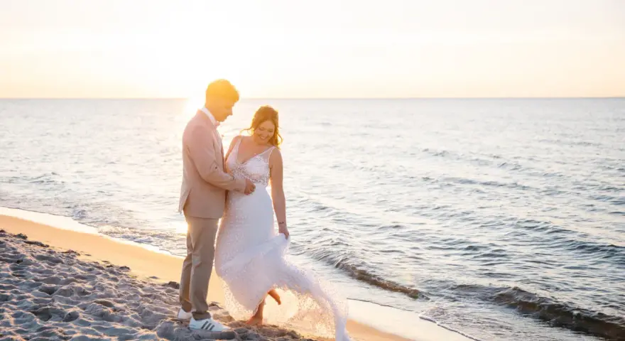 Ein glückliches Brautpaar feiert seine Hochzeit am Strand. Die Sonne geht unter und taucht die Szene in warmes Licht.