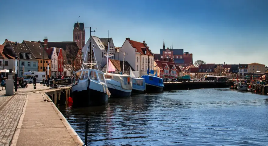 Boote liegen im **Wismar Hafen** vor bunten Häusern. Ein Schild wirbt für "Backfisch".