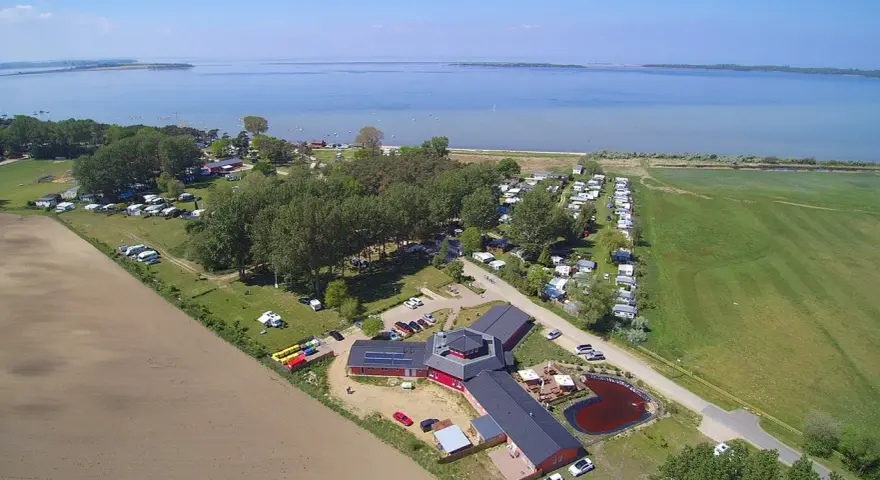 Luftaufnahme des pepelow campingplatzes mit Wohnmobilen, Bäumen und einem See im Hintergrund.