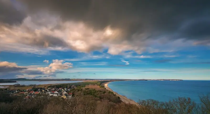 Blick vom Lotsenturm Thiessow über die Küste mit Dorf, Strand und Meer unter dramatischem Himmel.