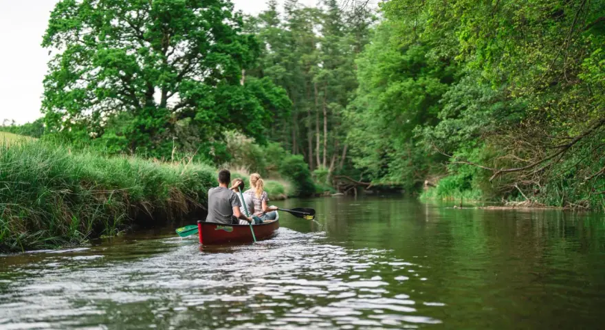 Ein Paar paddelt mit einem Kanu auf einem ruhigen Fluss durch üppige grüne Natur. Ein idyllischer Ausflug in Weitendorf.