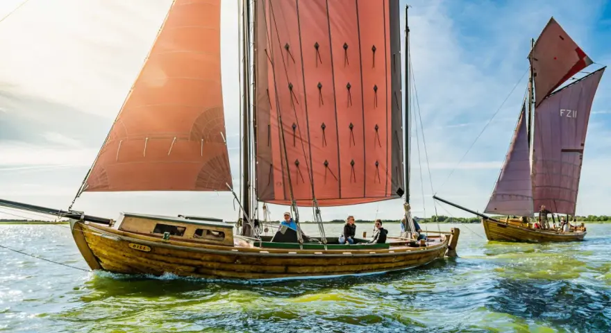 Zeesboot "Bill" segelt bei Ahrenshoop mit roten Segeln. Ein zweites Boot folgt.