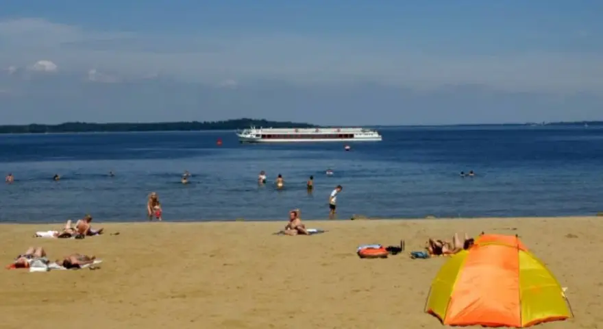 Sonne, Sand und ein Schiff auf dem Wasser – ein entspannter Tag am Schweriner Strand mit Badegästen und einer bunten Strandmuschel.
