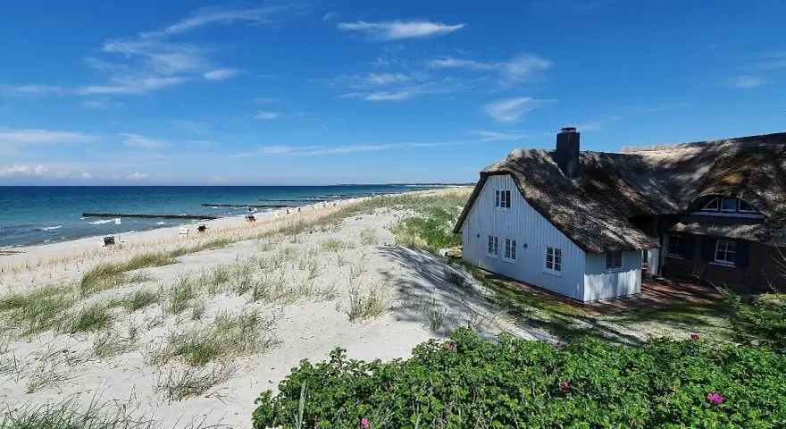 Ein reetgedecktes Haus am Strand von Ahrenshoop, mit Blick auf die Ostsee und den Sandstrand.