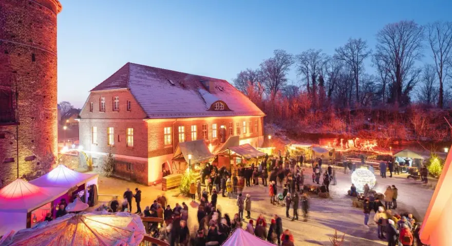 Belebter weihnachtsmarkt plau am see vor historischer Kulisse mit beleuchteten Buden und vielen Besuchern.