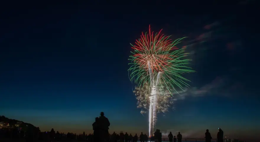 Silhouetten von Menschen am Strand beobachten ein beeindruckendes Feuerwerk über dem Meer. Ein leuchtendes Spektakel in Rot und Grün erhellt den Nachthimmel. Feuerwerk Usedom.
