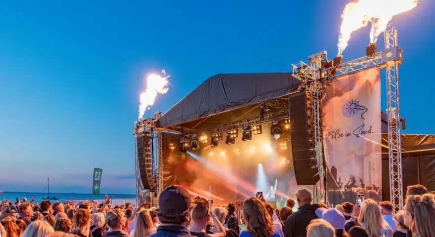 Feuerfontänen lodern bei Konzerten an der Ostsee. Eine Menschenmenge feiert am Strand zu elektronischer Musik.