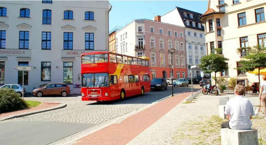 Roter Doppeldeckerbus für eine Stadtrundfahrt in Rostock fährt durch eine Gasse mit historischen Gebäuden.