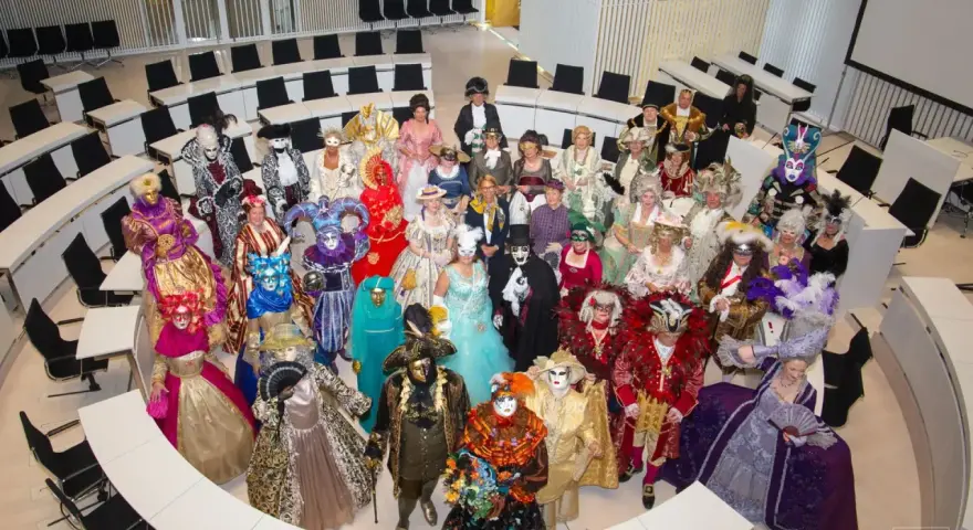 Eine Gruppe in prächtigen Kostümen und Masken, die an venezianische Tage in Schwerin erinnert, versammelt sich in einem modernen Sitzungssaal.