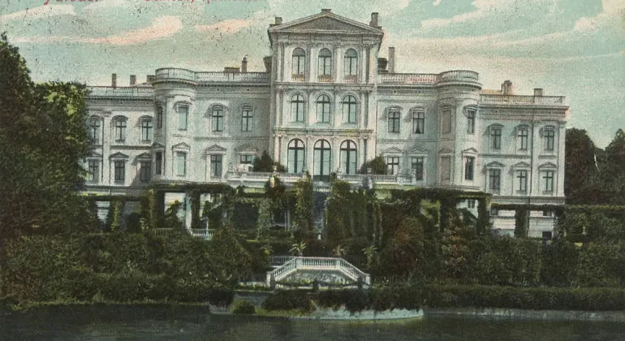 Das Schloss Putbus, von der Rückseite betrachtet, thront majestätisch über einem üppigen Garten und einem ruhigen Gewässer.