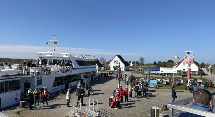 Menschen warten am Kai in Neuendorf auf Hiddensee auf die Fähre. Ein großes Ausflugsschiff liegt bereit.