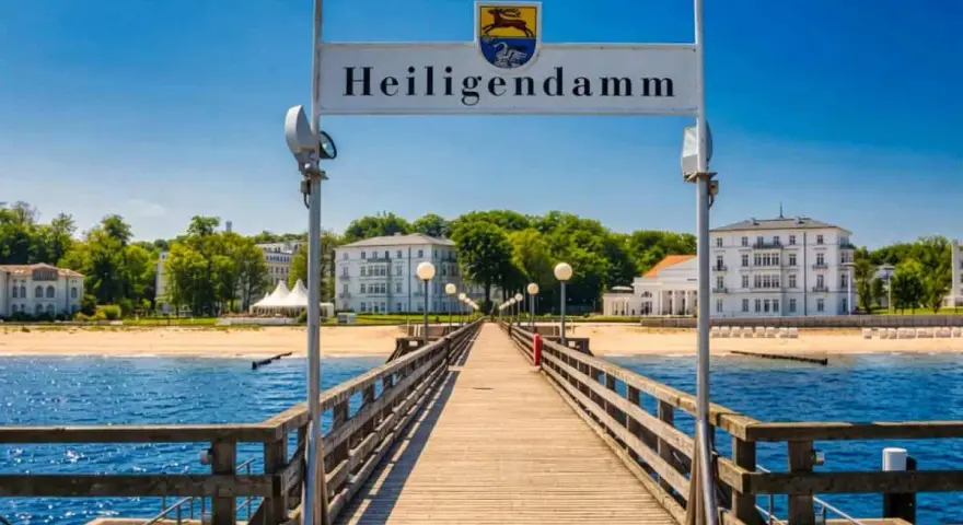 Holzsteg führt zum Heiligendamm Strand mit weißen Gebäuden und blauem Himmel.