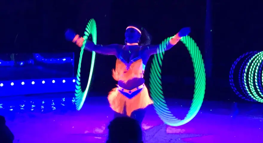 Artistin dreht leuchtende Reifen auf der Bühne des Circus Moreno. Neonfarben und Schwarzlicht erzeugen eine magische Atmosphäre.
