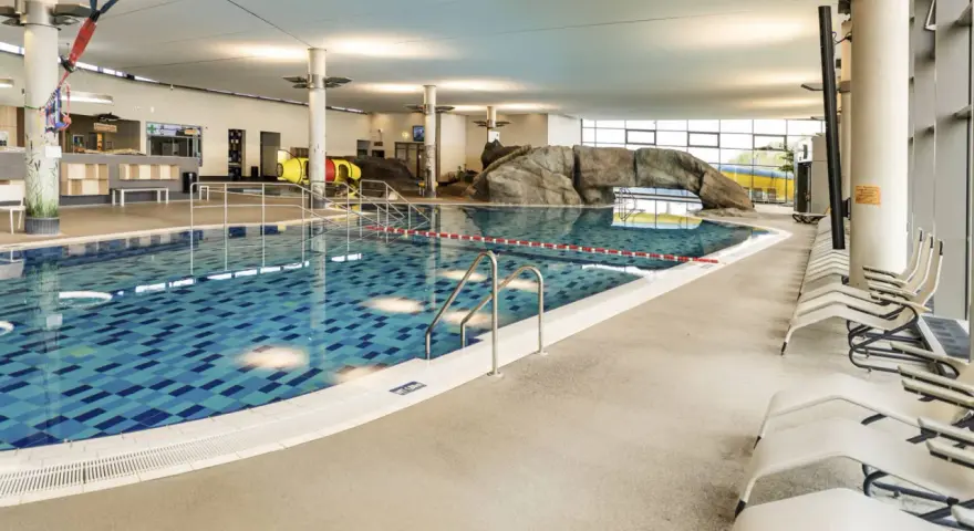 Ein großes Schwimmbecken mit blauen Kacheln und einer Felswand lädt zum Badespaß ein. Hier ist das perfekte Erlebnisbad Ostsee für die ganze Familie.