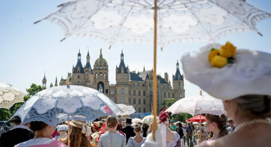 Besucher im historischen Gewand mit Sonnenschirmen beim Altstadtfest Schwerin vor dem Schloss.
