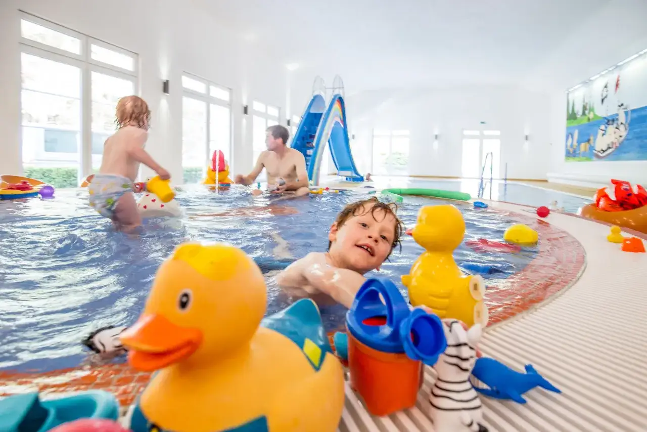 Kinder planschen im Ostsee Schwimmbad mit Enten und Rutsche. Ein Junge lacht in die Kamera.