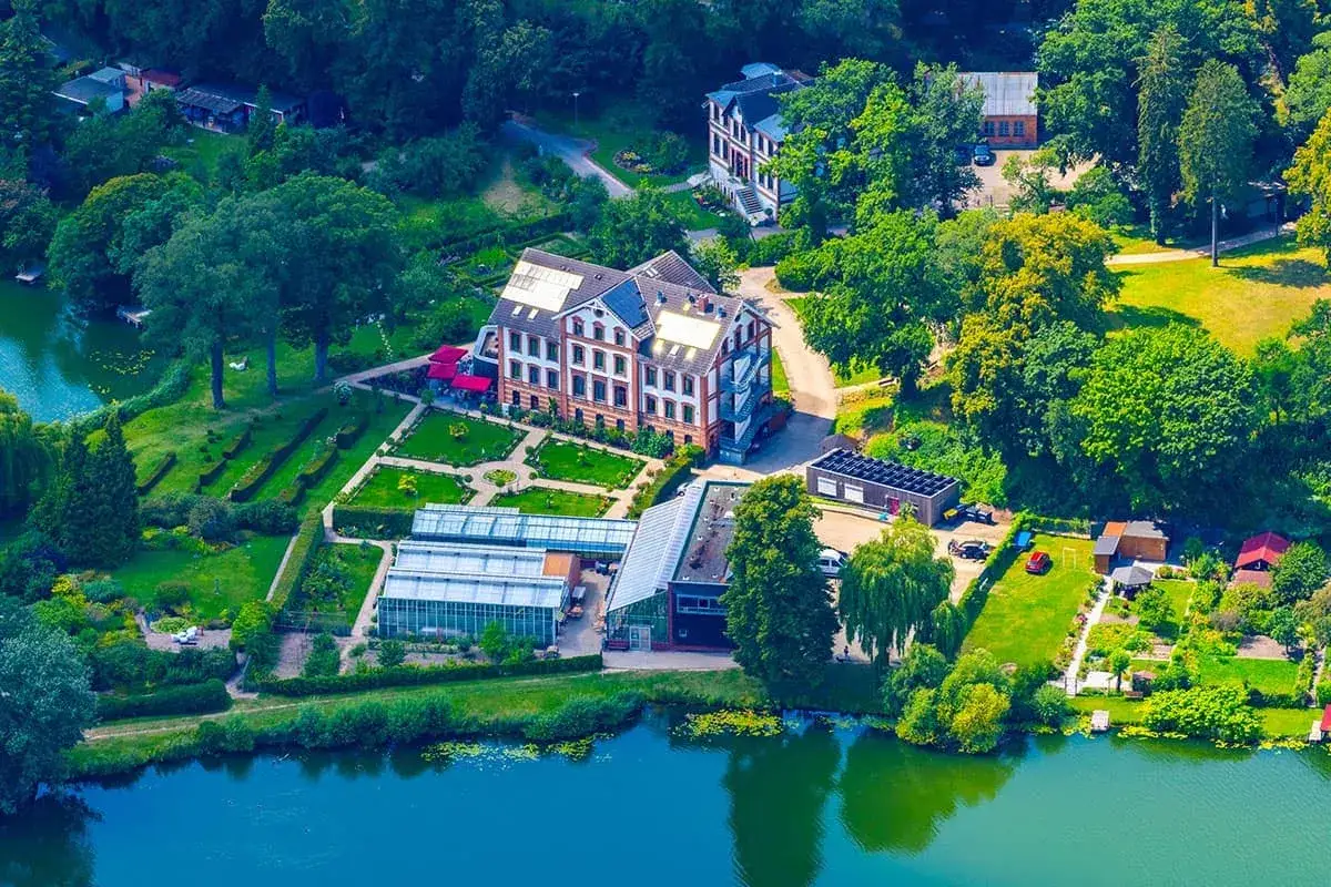 Luftaufnahme des schaugarten am tiefwarensee mit Gew&auml;chsh&auml;usern, einem Hauptgeb&auml;ude und einem See.