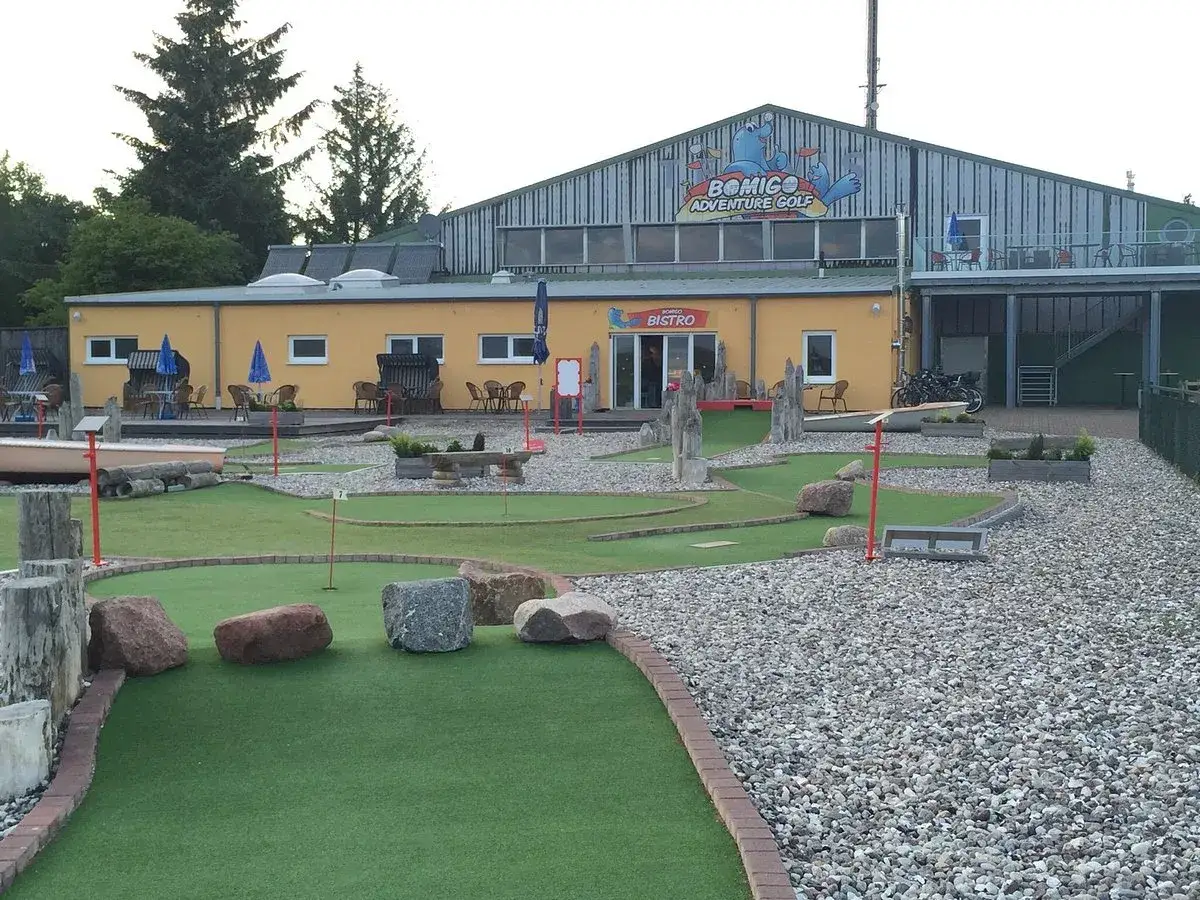 BOMIGO Adventure Golf Zingst: Eine Minigolfanlage mit Bistro, umgeben von Kies und gr&uuml;nen Kunstrasenbahnen.