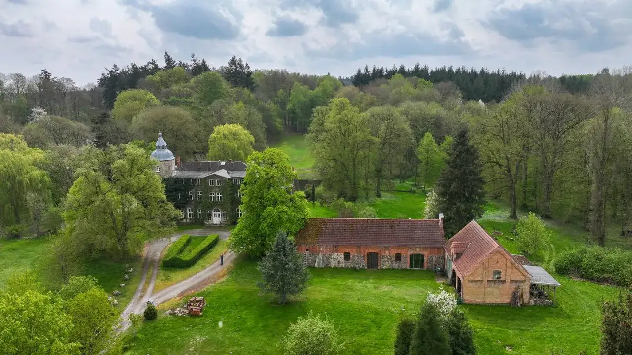 Das Gutshaus Wesselstorf, umgeben von üppigem Grün und alten Bäumen, zeigt seine historische Architektur unter einem bewölkten Himmel.