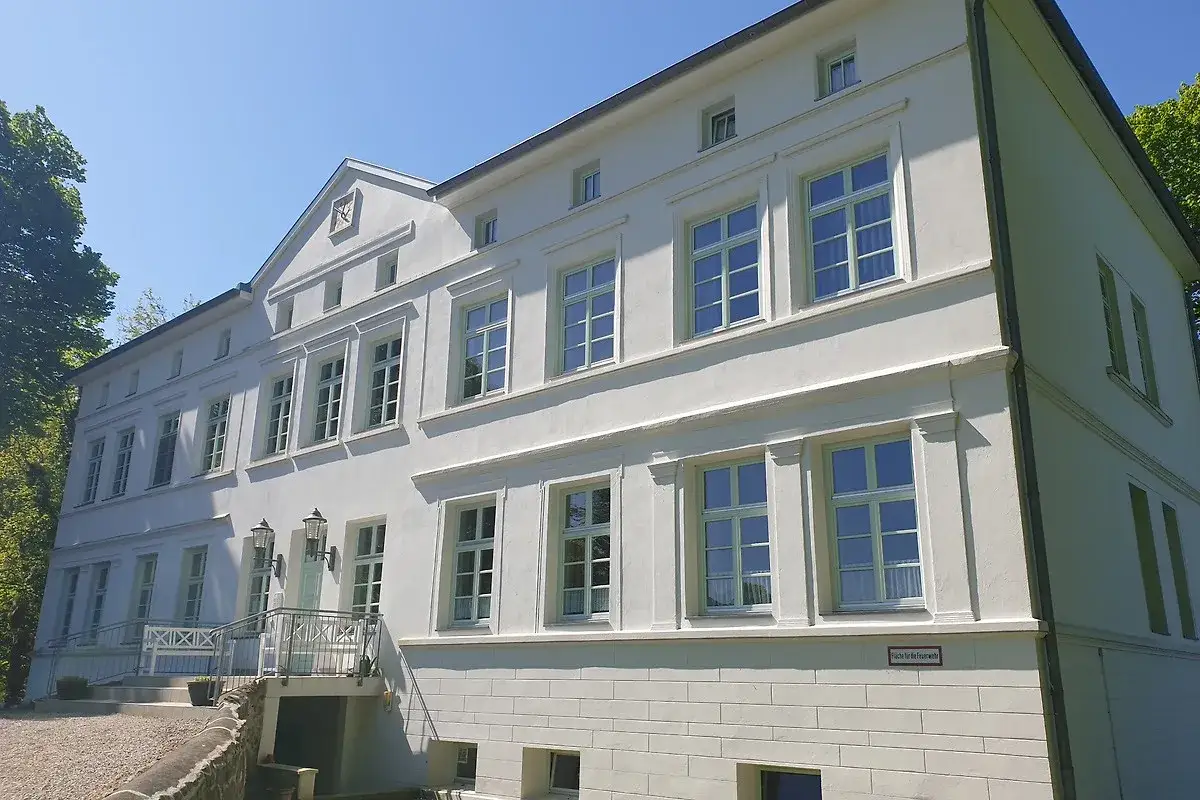 Das Herrenhaus Blengow, ein wei&szlig;es Geb&auml;ude mit vielen Fenstern, steht unter blauem Himmel.