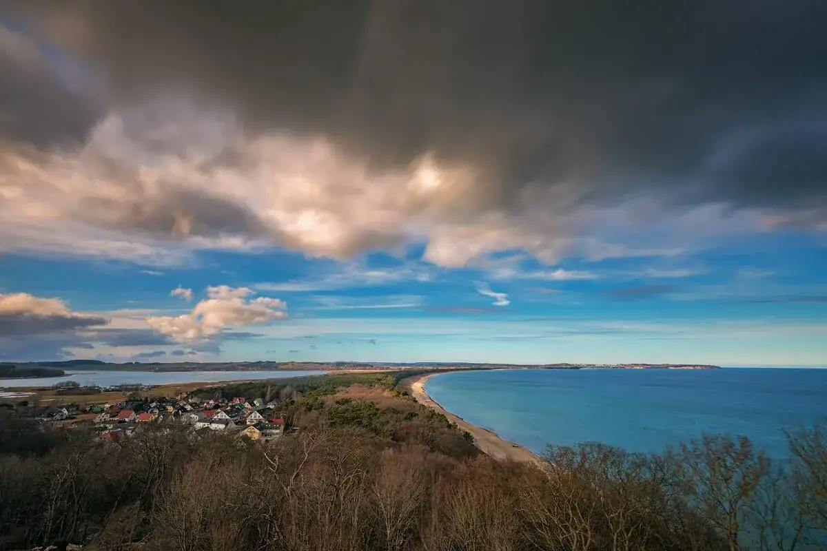 Blick vom Lotsenturm Thiessow &uuml;ber die K&uuml;ste mit Dorf, Strand und Meer unter dramatischem Wolkenhimmel.