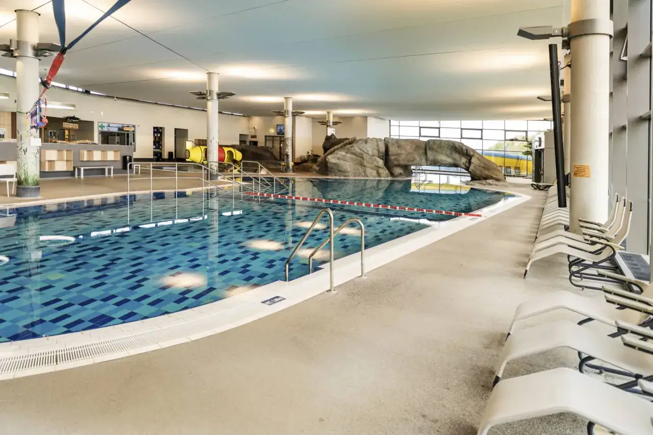 Ein gro&szlig;es Schwimmbecken mit blauen Kacheln und einer Felswand-Attraktion. Hier ist das perfekte Erlebnisbad Ostsee f&uuml;r die ganze Familie.