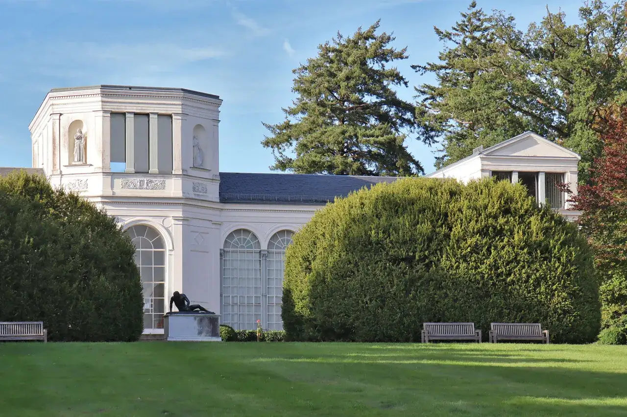 Das Schloss Putbus, ein klassizistisches Geb&auml;ude, umgeben von &uuml;ppigem Gr&uuml;n und einem Denkmal.