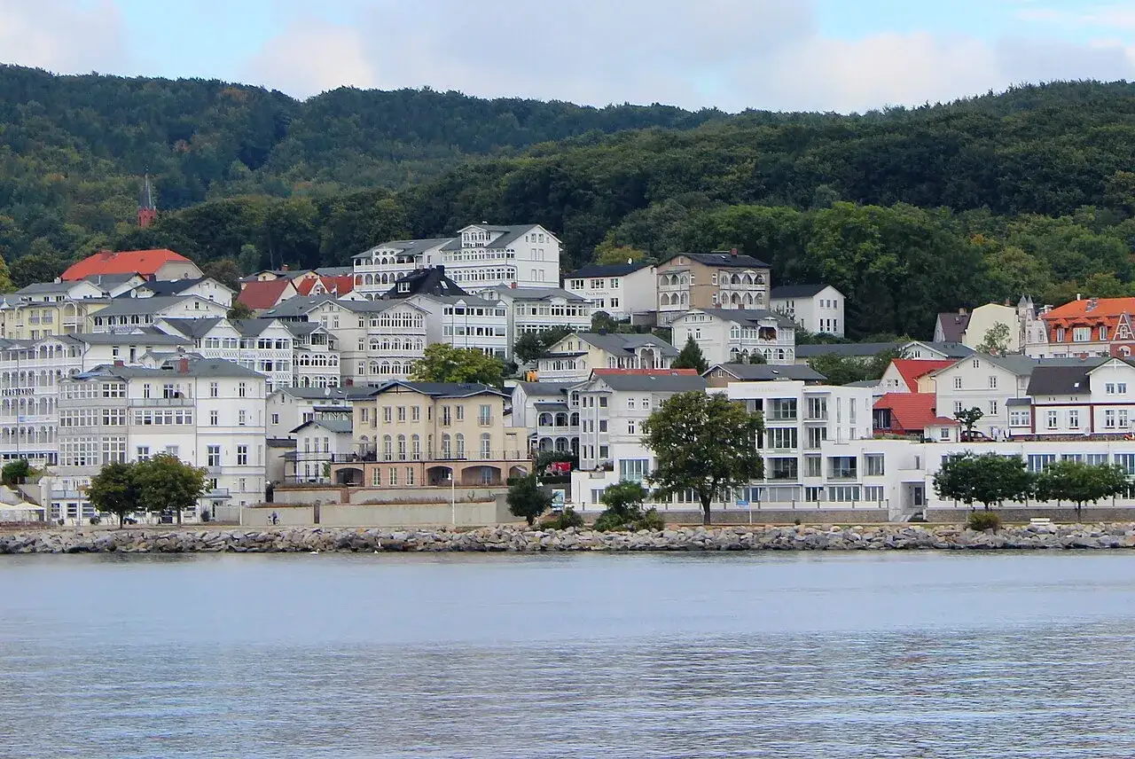 Blick auf die Küstenstadt Sassnitz mit weißen Häusern und grünen Hügeln im Hintergrund.
