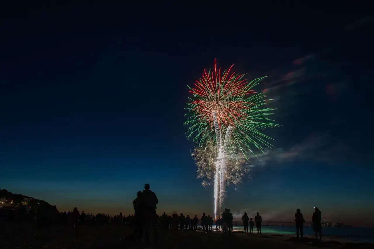 Silhouetten von Menschen am Strand beobachten ein spektakul&auml;res Feuerwerk &uuml;ber dem Meer. Ein unvergesslicher Abend mit Feuerwerk Usedom.