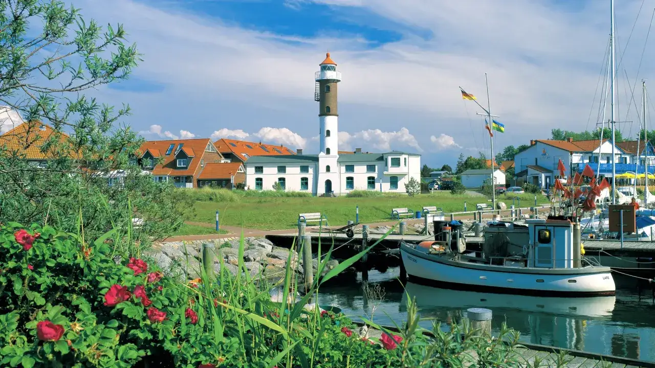 Idyllischer Hafen mit Leuchtturm auf Insel Poel, ein echter Geheimtipp. Boote liegen im Wasser, rote Rosen bl&uuml;hen.