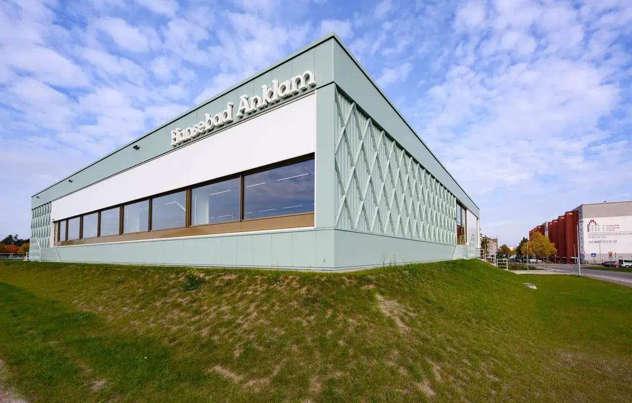 Moderne Architektur der Schwimmhalle Anklam mit großflächigen Fenstern und einem hellgrünen Fassadendesign unter blauem Himmel.