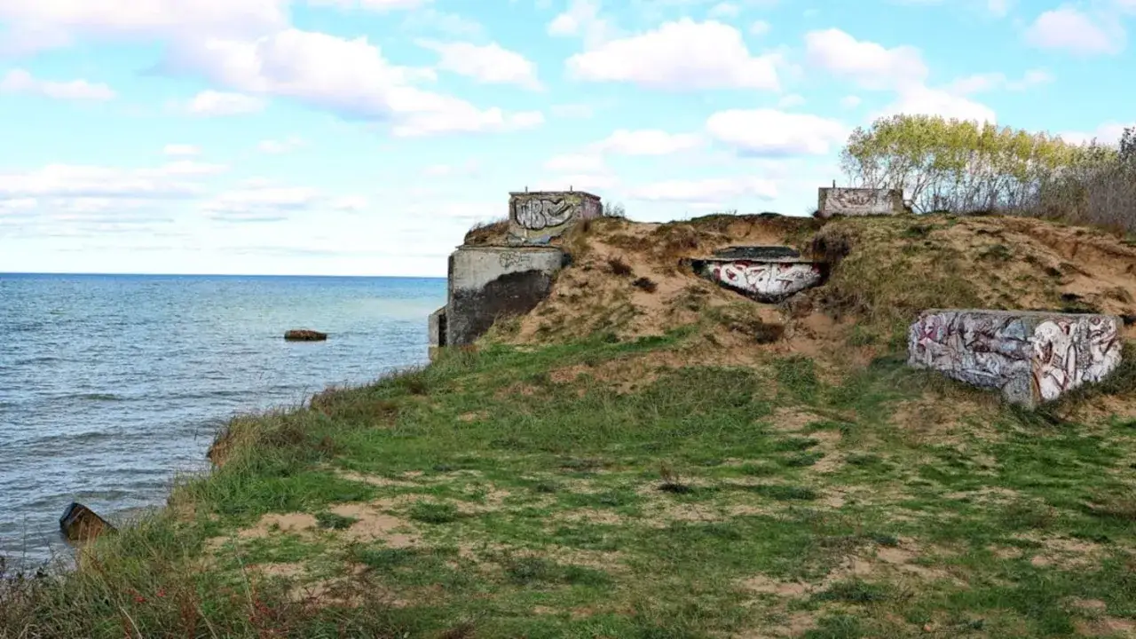 Verwitterter bunker am strand, mit Graffiti bemalt, thront auf einer sandigen D&uuml;ne &uuml;ber dem Meer.